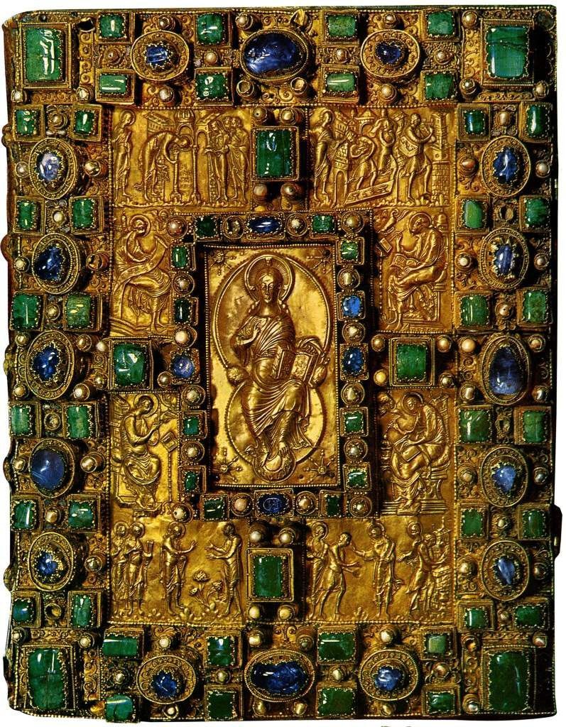 The front cover of a manuscript: a gold panel worked in high relief with a seated central figure in a frame, surrounded by smaller figured panels, set with numerous cut gemstones and pearls in raised mounts.